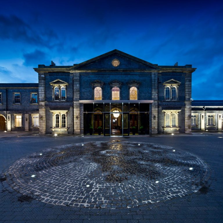 Historic building at twilight with a cobblestone courtyard and illuminated entrance.